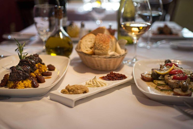 Multiple plated dishes with white wine and basket of bread
